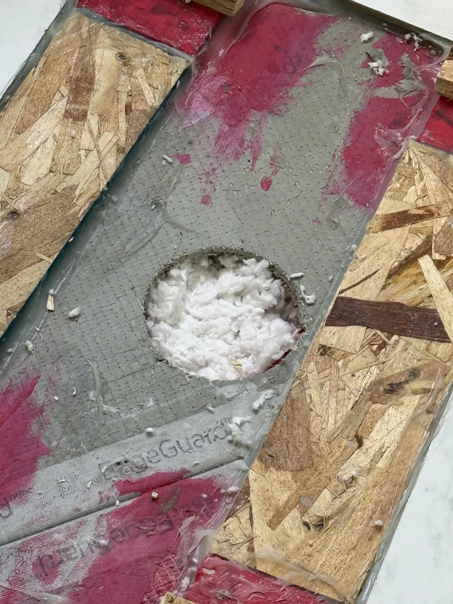 Close up of a red waterproofing membrane board with a round cut-out packed with insulation around a pipe