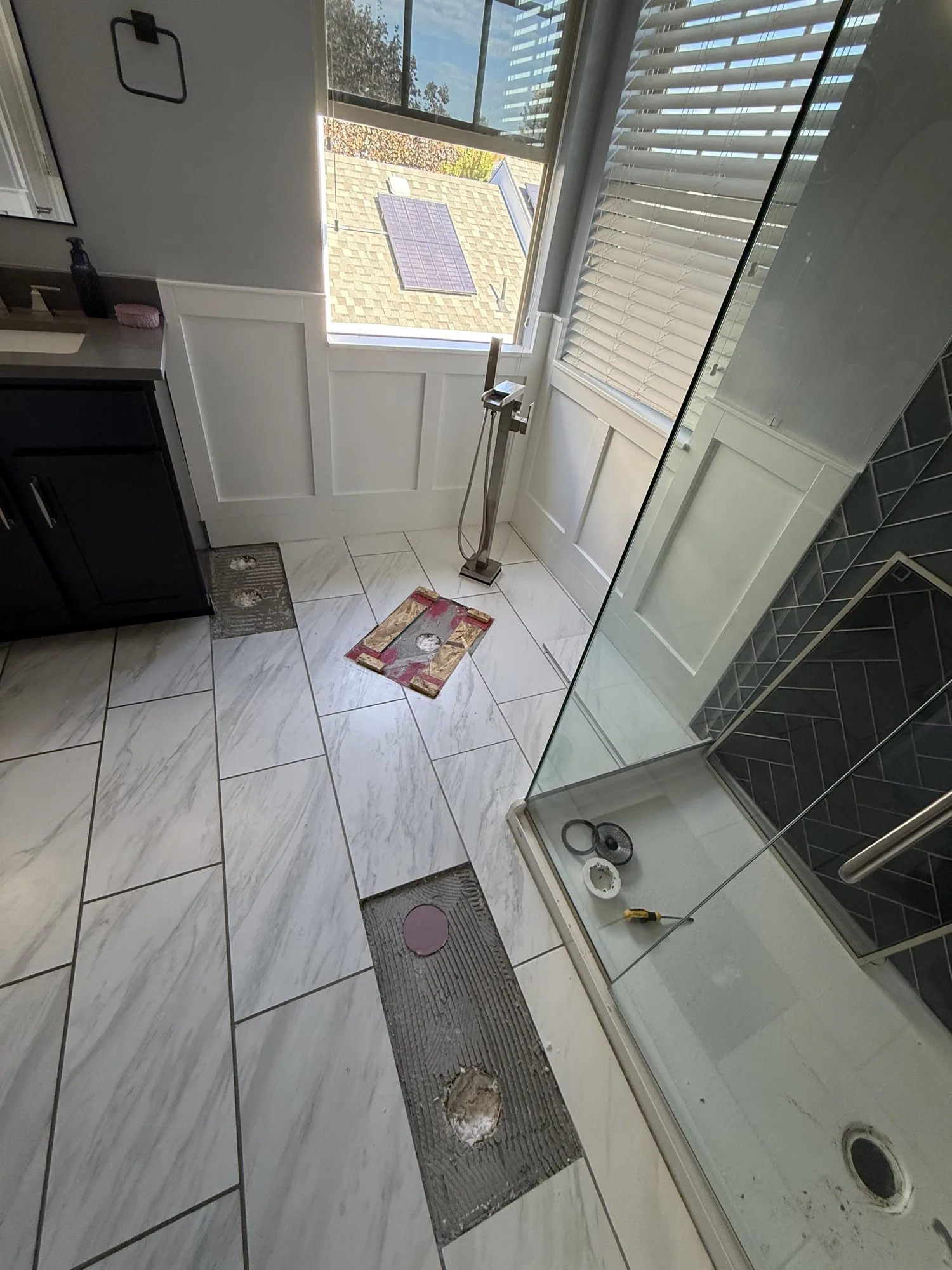 Finished bathroom with a tiled floor and glass shower, with floor patches by the vanity and the shower entry