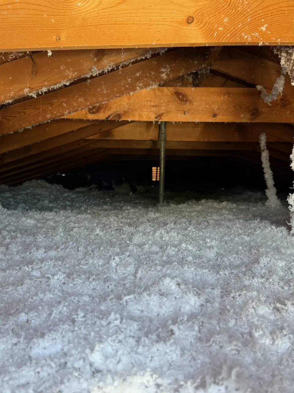 Attic floor under the same wood trusses covered in an even layer of white blown insulation
