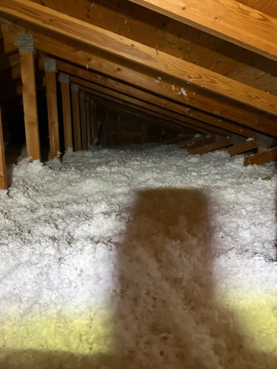 The same attic with white blown insulation filled in level between the trusses