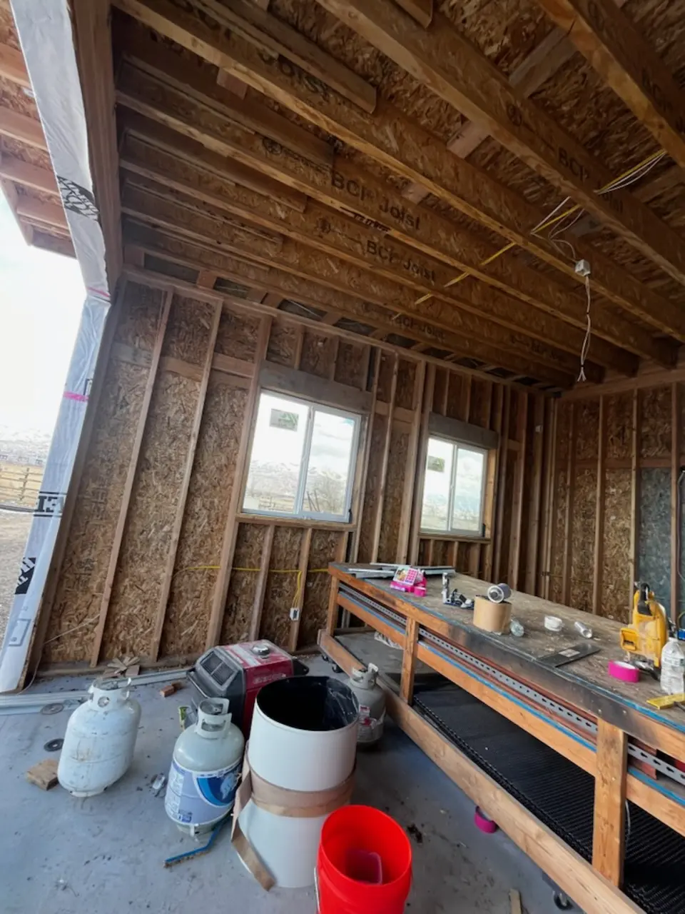 Framed room with bare wood studs and OSB sheathing, two windows and a long work bench